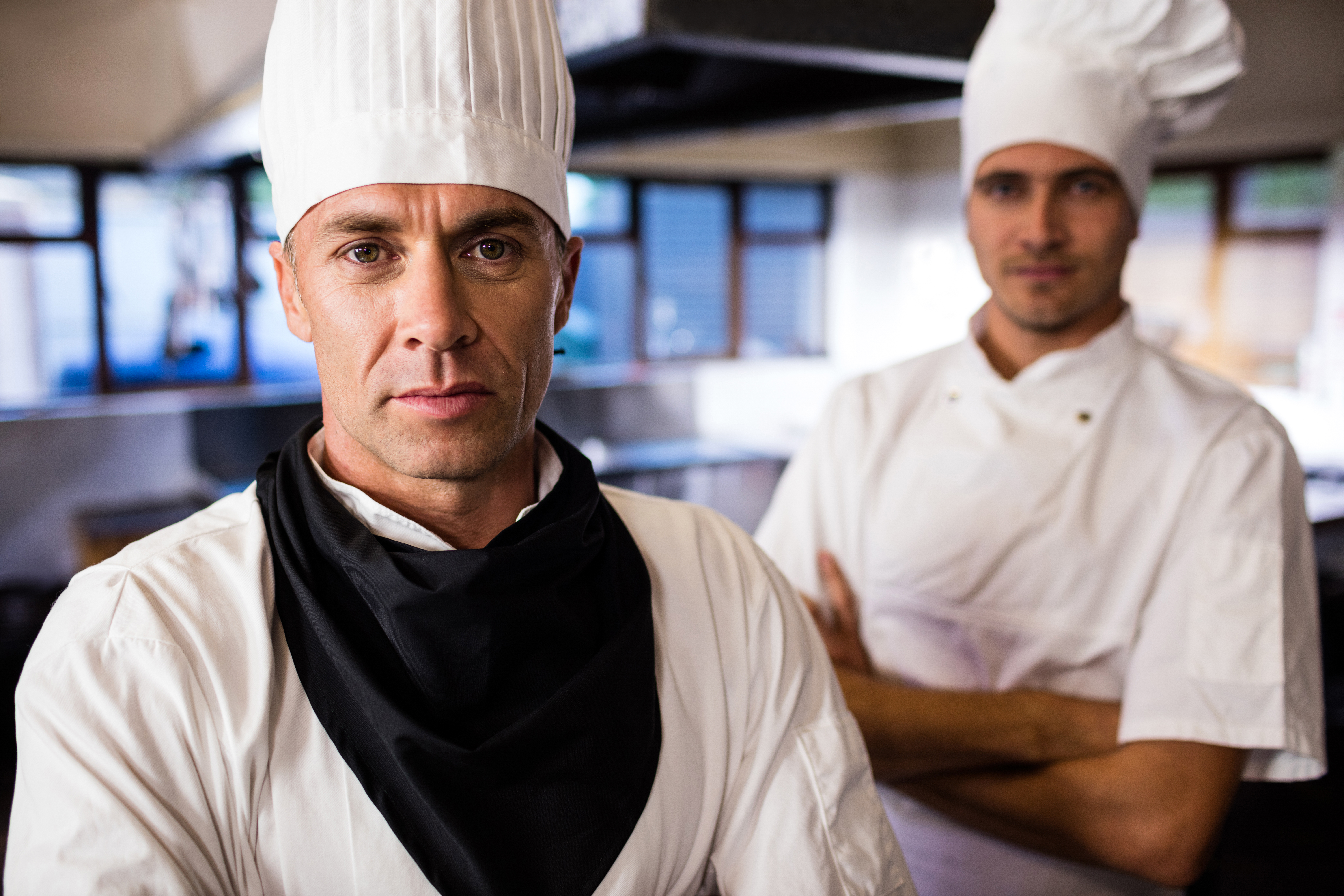 Two male chefs standing with arms crossed in kitchen at hotel
